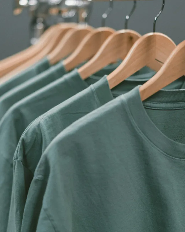 Camisetas color salvia colgadas en ganchos de madera